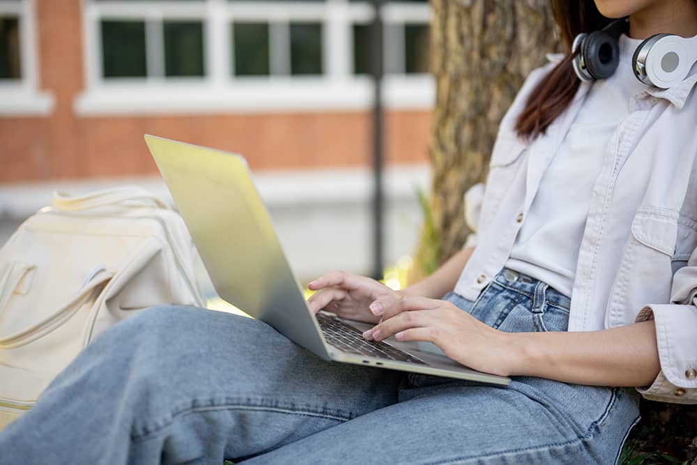 Vista recortada lateral de una mujer trabajando en su computadora portátil bajo un árbol en un parque