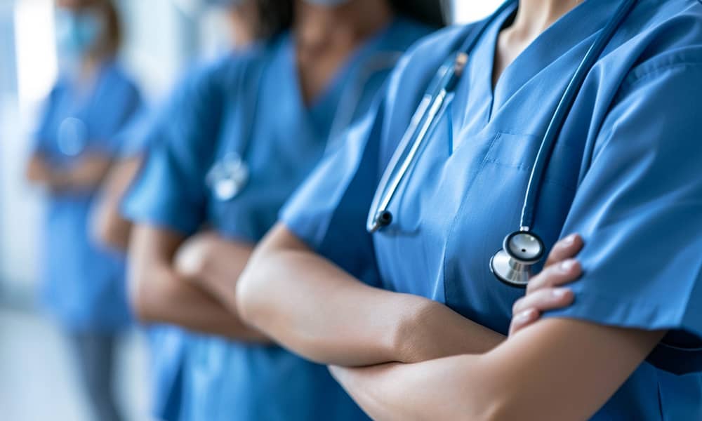 grado-enfermeria-1 Enfermeras alineadas con los brazos cruzados, reflejando compromiso y solidaridad en su profesión de atención médica.