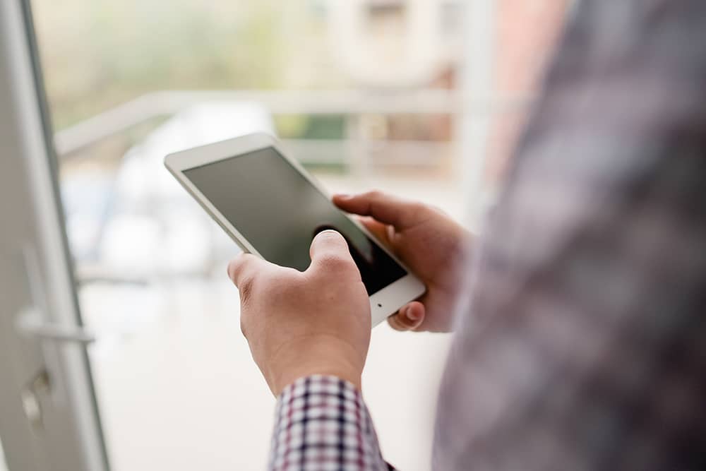 control-asistencia Sección media de un hombre usando un teléfono móvil junto a la ventana